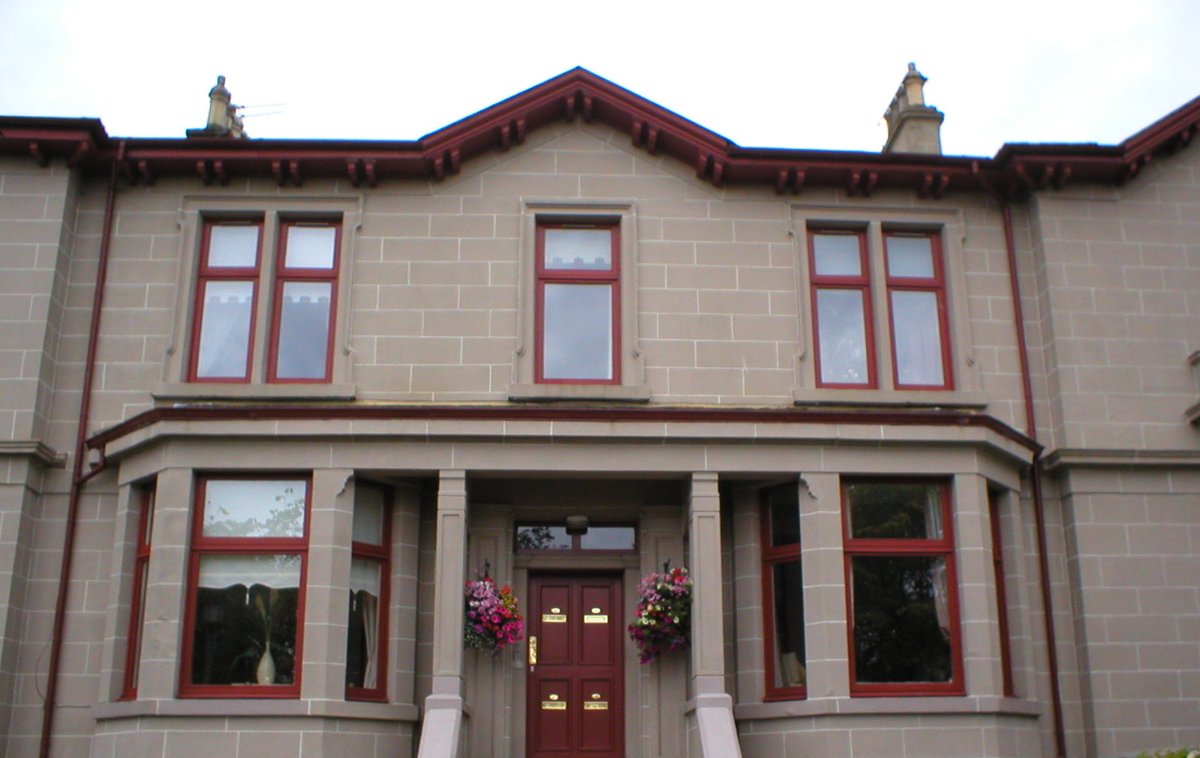 Red-brown window frames on the front of a traditional stone house.