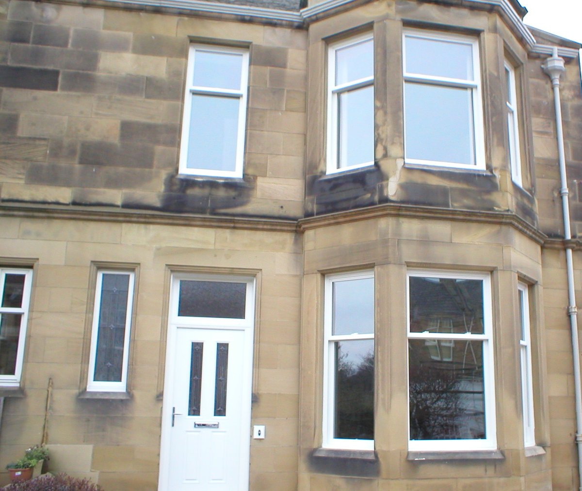 White bay windows and a white entrance door on a stone house.